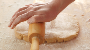 Hard biscuit dough rolled out on a surface with a rolling pin.