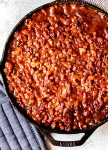 Rustic skillet of baked beans topped with bacon and parsley.