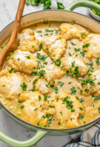 A bowl of thick, creamy chicken and dumplings with garnished parsley.