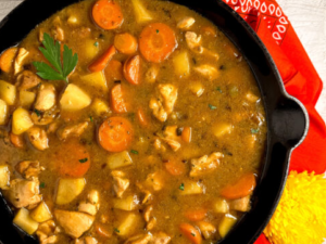 A whisk stirring roux into a pot of chicken stew.