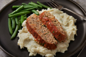 Sliced meat loaf served with mashed potatoes and green beans.